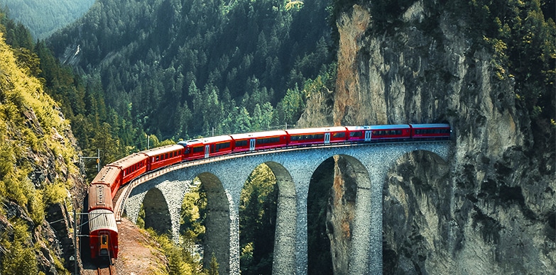 A train passing through a scenic location featuring a breathtaking bridge and its surroundings.